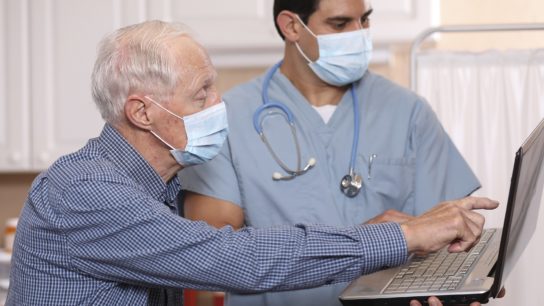 Doctor and patient wearing masks looking at laptop