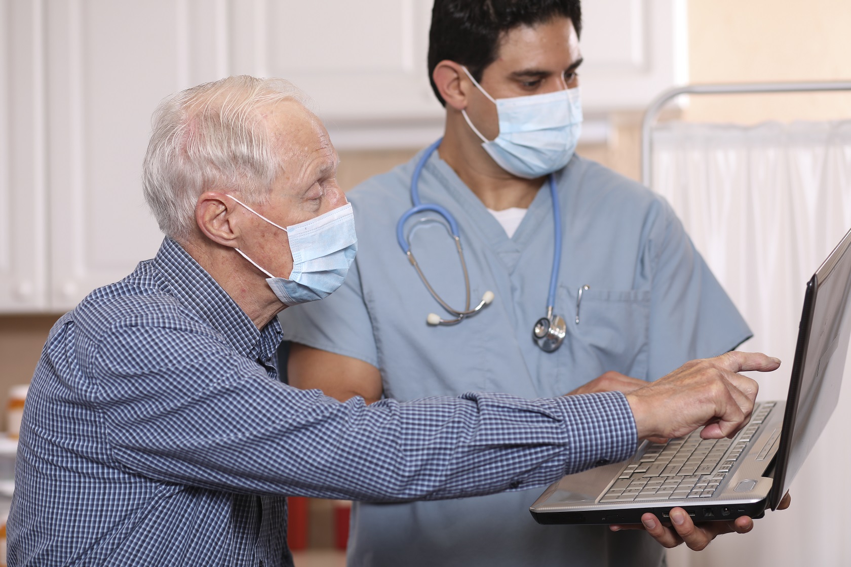 Doctor and patient wearing masks looking at laptop