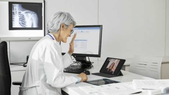 Female doctor waving hand while giving telehealth consult