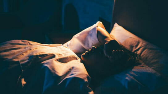 Young_woman_ lying_on_bed_with_ hand_on_forehead.