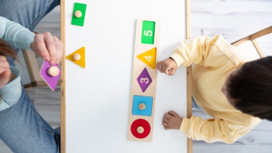 Top-view-of-a-female-therapist-and-autistic-boy-playing-skill-games-in-nursery