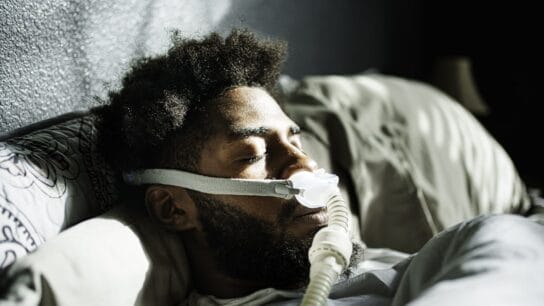 Athletic Young African American Man in His Twenties Sleeping Peacefully Using a CPAP Machine (contenuous positive air pressure) in a Dark Bedroom